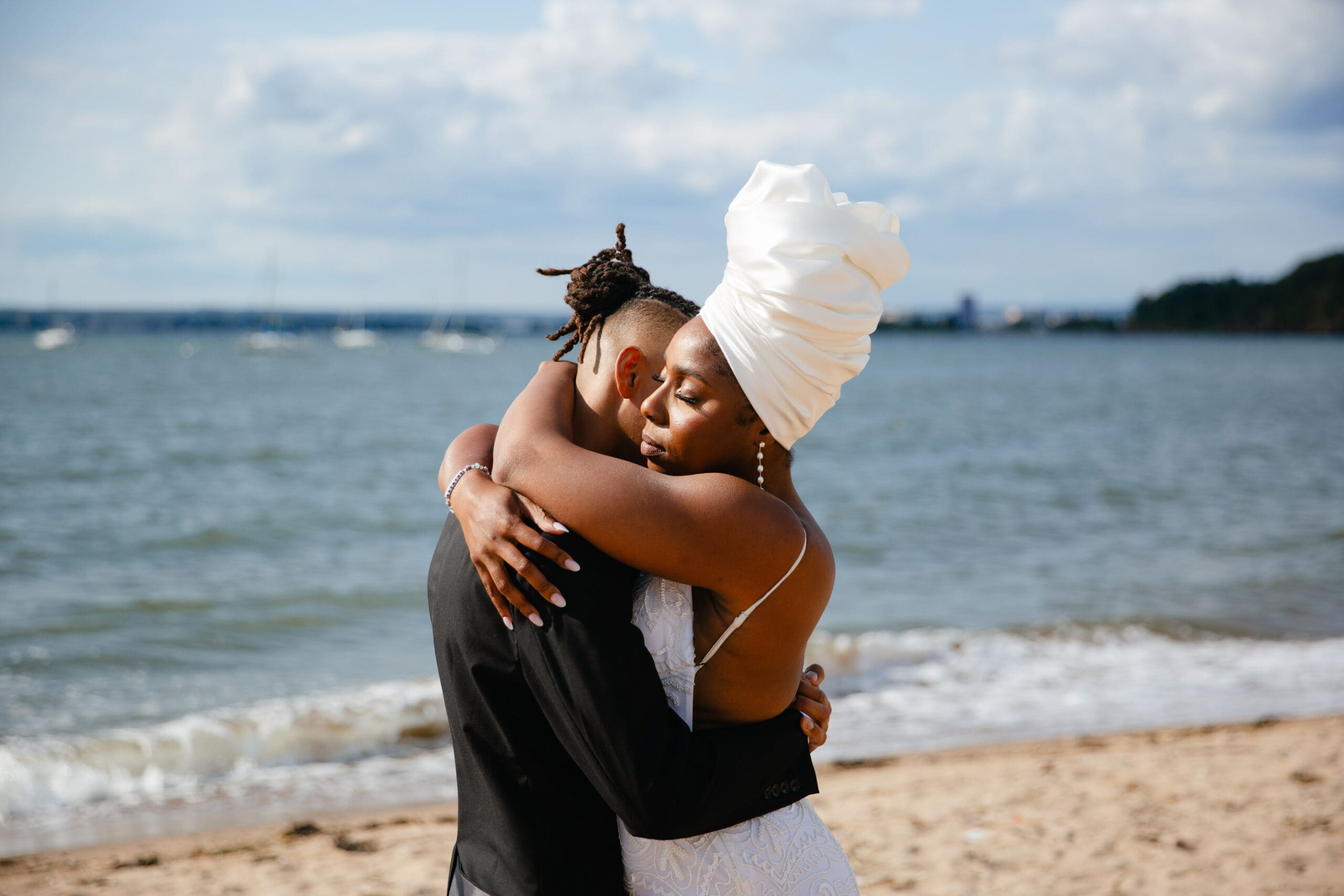 bride and grom embracing with new havens shoreline behind them