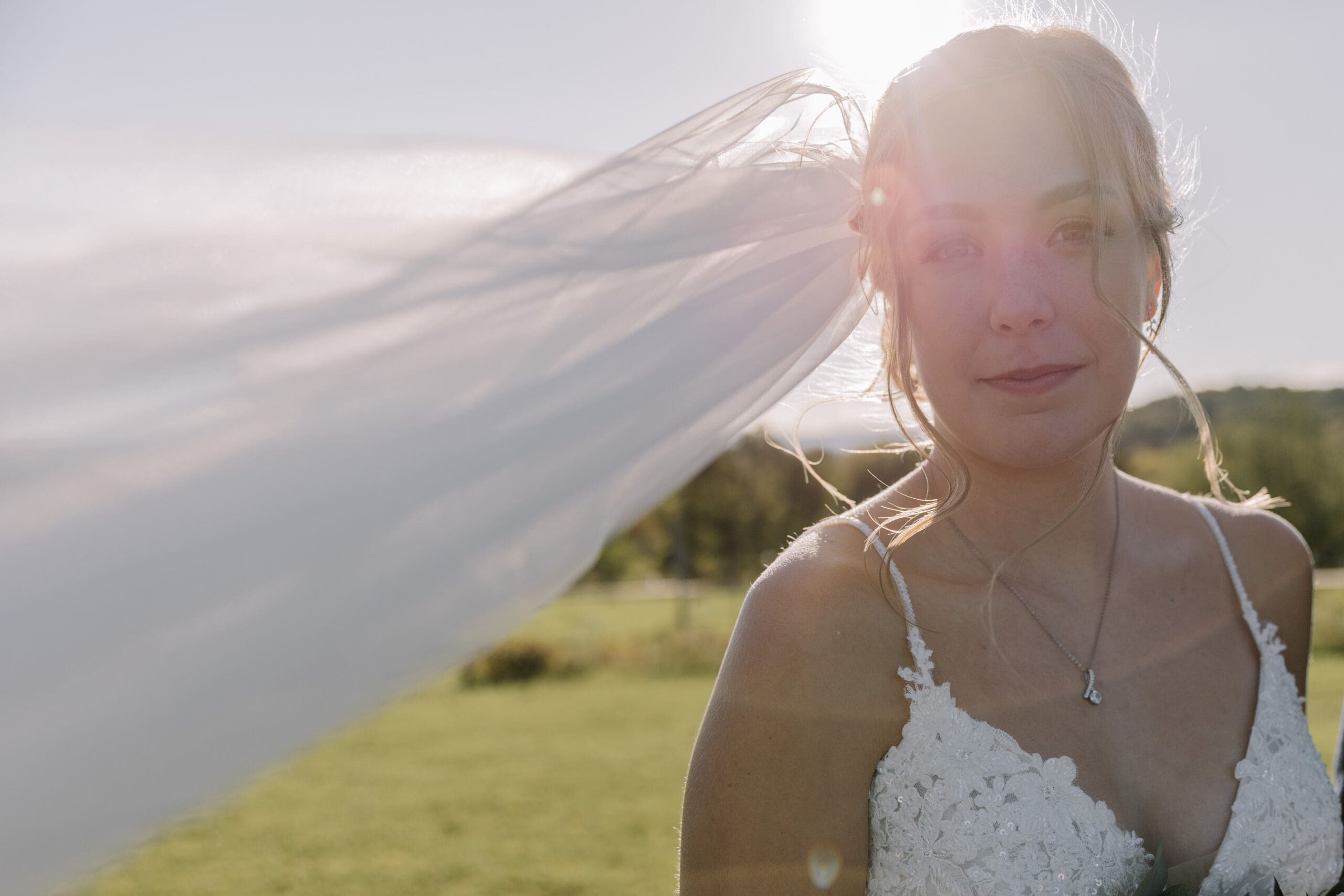Bride softly smiling while veil blows in the wind to her right